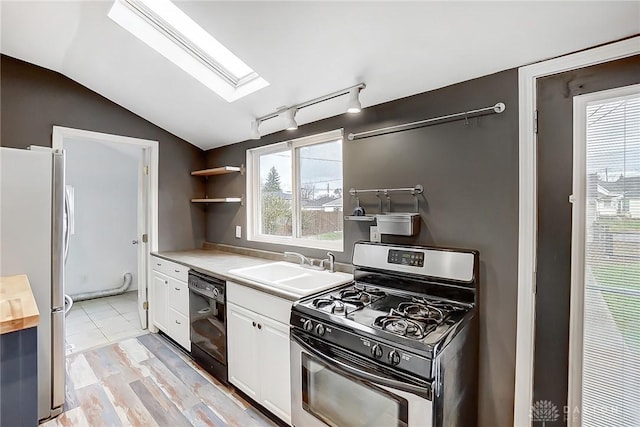 kitchen featuring sink, appliances with stainless steel finishes, vaulted ceiling with skylight, light hardwood / wood-style floors, and white cabinets