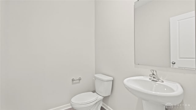 half bathroom with baseboards, a sink, and toilet