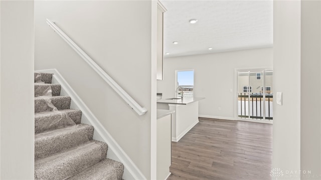 staircase featuring baseboards, wood finished floors, and recessed lighting