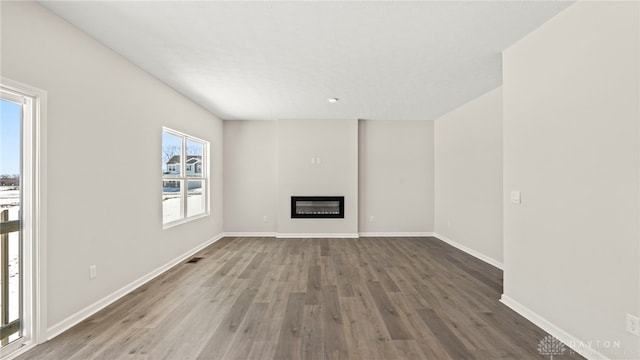 unfurnished living room featuring wood finished floors, a glass covered fireplace, visible vents, and baseboards