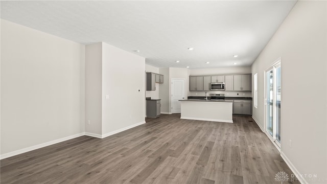 kitchen featuring a center island with sink, gray cabinets, appliances with stainless steel finishes, wood finished floors, and baseboards