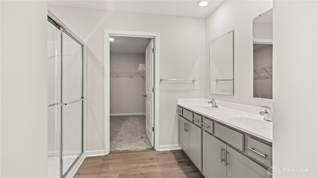 full bathroom with wood finished floors, a sink, baseboards, a shower stall, and double vanity