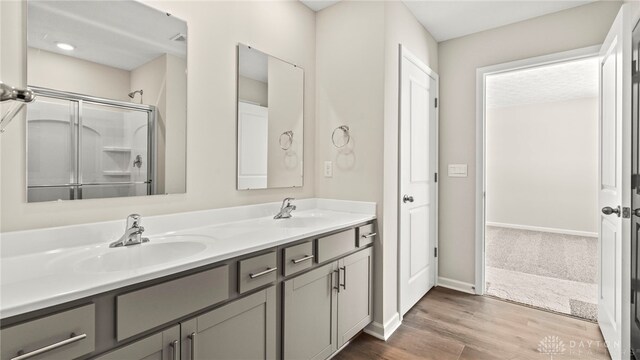 bathroom with double vanity, baseboards, wood finished floors, an enclosed shower, and a sink