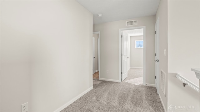 hall featuring light colored carpet, visible vents, and baseboards