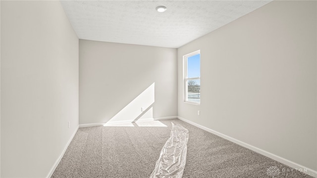 spare room with carpet, baseboards, and a textured ceiling