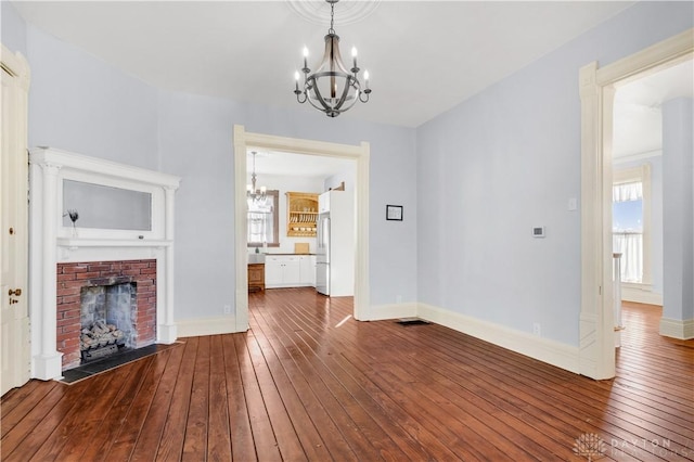 unfurnished living room featuring a fireplace, wood-type flooring, and a notable chandelier