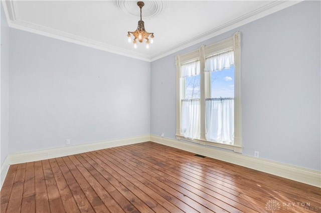 empty room featuring hardwood / wood-style flooring, an inviting chandelier, and ornamental molding