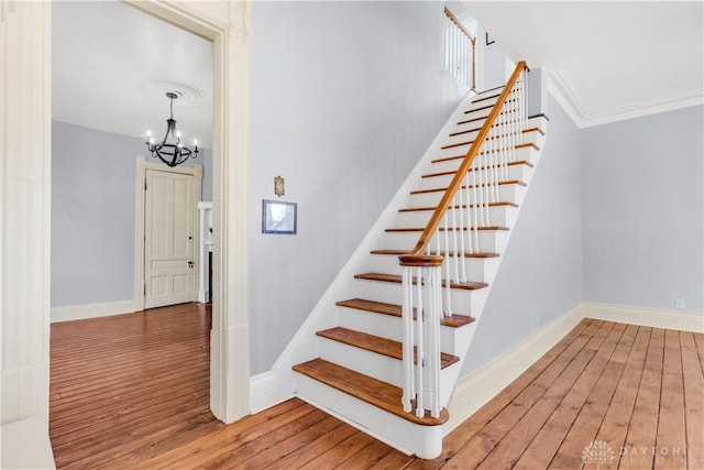 stairway with crown molding, a notable chandelier, and hardwood / wood-style flooring