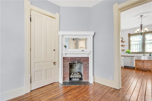 unfurnished living room with light wood-type flooring, an inviting chandelier, a brick fireplace, and sink