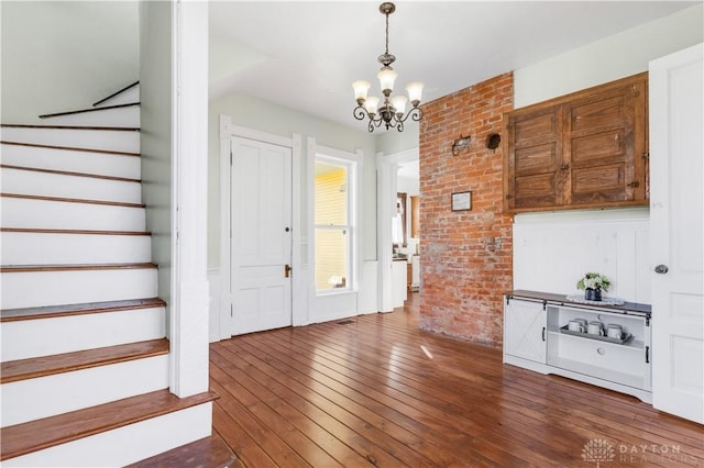 foyer entrance featuring a chandelier, dark hardwood / wood-style flooring, and brick wall