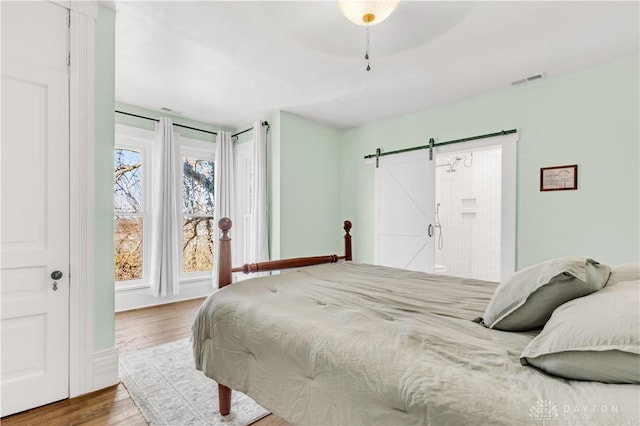 bedroom with a barn door, ceiling fan, and wood-type flooring