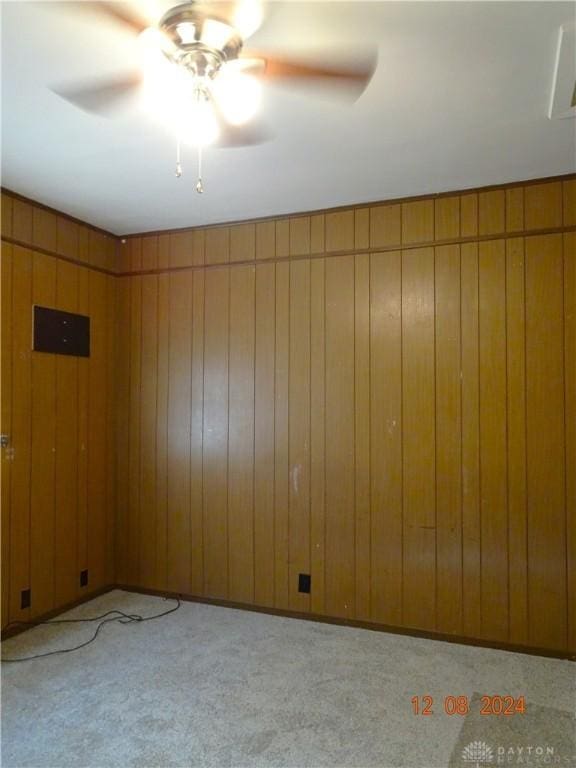 empty room with ceiling fan, light colored carpet, and wood walls