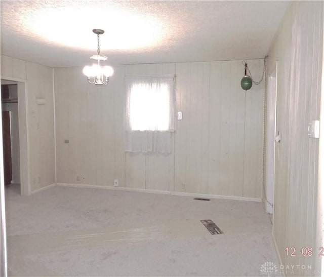 spare room with a textured ceiling, wooden walls, and a notable chandelier