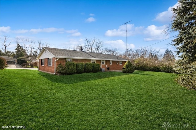 view of side of property with cooling unit, brick siding, and a yard