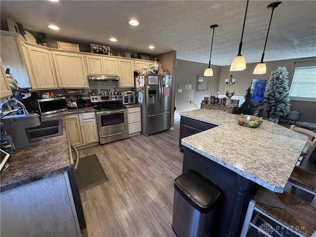 kitchen with dark hardwood / wood-style flooring, stainless steel appliances, a center island, hanging light fixtures, and a breakfast bar area