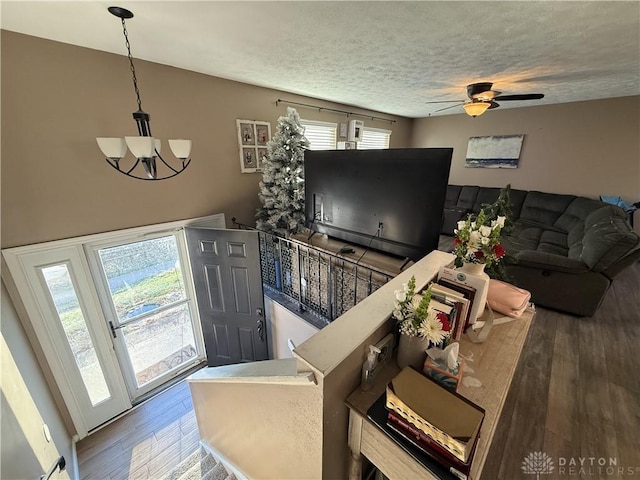 living room featuring a textured ceiling, ceiling fan with notable chandelier, a wealth of natural light, and dark wood-type flooring