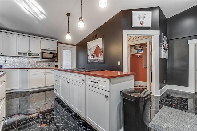 kitchen with decorative backsplash, vaulted ceiling, built in microwave, decorative light fixtures, and white cabinetry