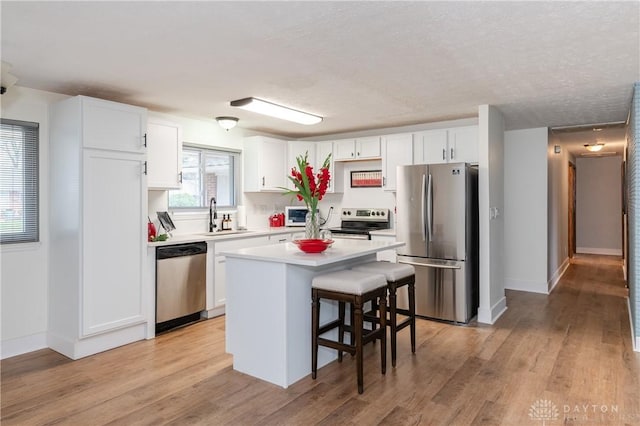 kitchen with a kitchen bar, appliances with stainless steel finishes, light hardwood / wood-style flooring, white cabinets, and a kitchen island