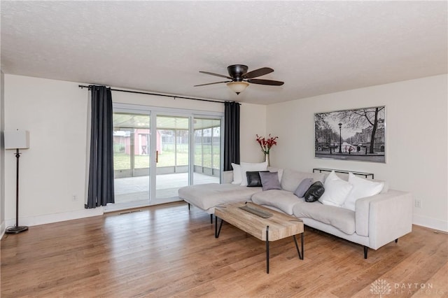 living room featuring ceiling fan, light wood-type flooring, and a textured ceiling