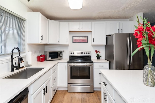 kitchen with appliances with stainless steel finishes, a textured ceiling, sink, light hardwood / wood-style flooring, and white cabinetry