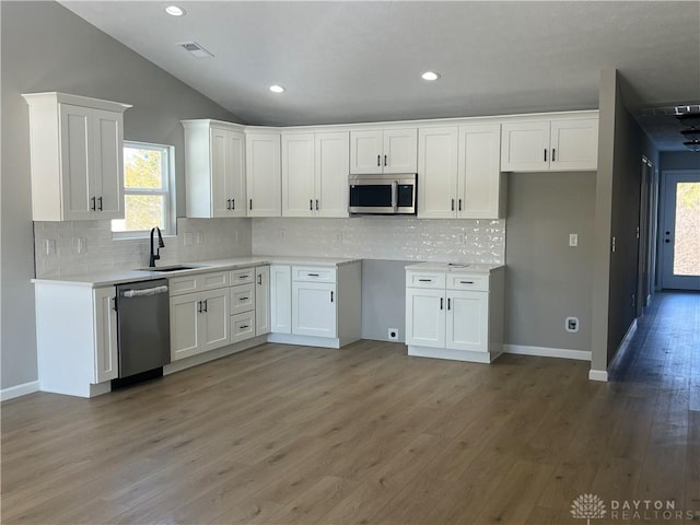 kitchen featuring sink, appliances with stainless steel finishes, white cabinets, hardwood / wood-style floors, and backsplash