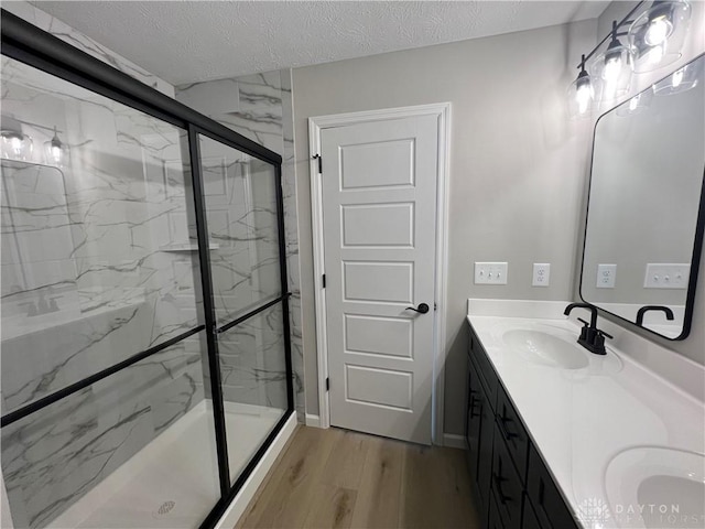 bathroom featuring vanity, wood-type flooring, a shower with door, and a textured ceiling