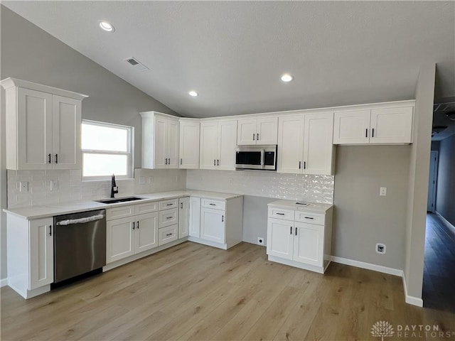 kitchen with sink, white cabinetry, vaulted ceiling, stainless steel appliances, and light hardwood / wood-style floors