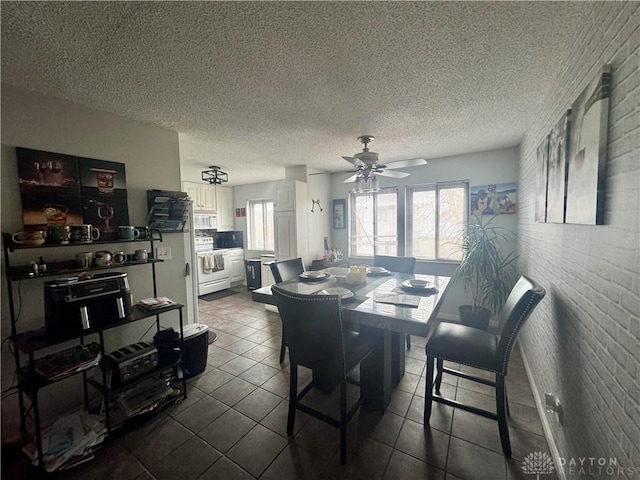 dining space with ceiling fan, brick wall, dark tile patterned flooring, and a textured ceiling