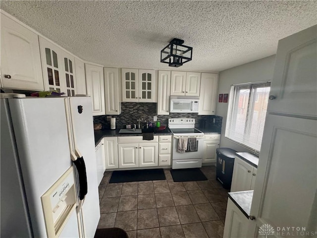 kitchen with tasteful backsplash, white cabinets, dark tile patterned flooring, and white appliances