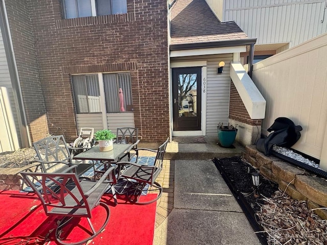 doorway to property featuring a shingled roof, outdoor dining area, a patio area, and brick siding