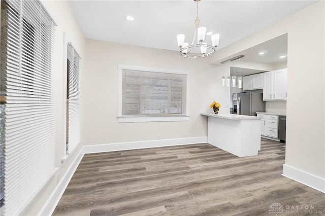 kitchen featuring stainless steel appliances, wood-type flooring, a notable chandelier, white cabinets, and hanging light fixtures