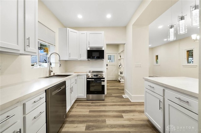 kitchen with stainless steel appliances, sink, decorative light fixtures, light hardwood / wood-style floors, and white cabinetry