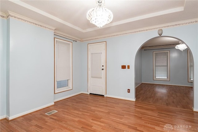 spare room with a tray ceiling, crown molding, light hardwood / wood-style flooring, and a notable chandelier