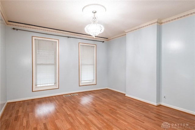 empty room featuring crown molding, light hardwood / wood-style flooring, and a notable chandelier