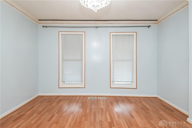 empty room with a notable chandelier, crown molding, and light hardwood / wood-style flooring