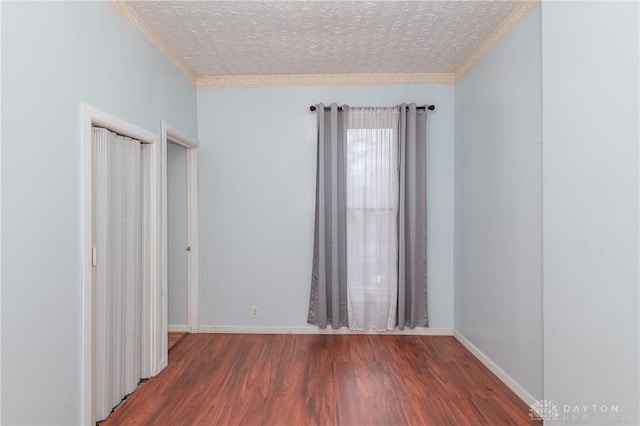 empty room with a textured ceiling, crown molding, and dark wood-type flooring