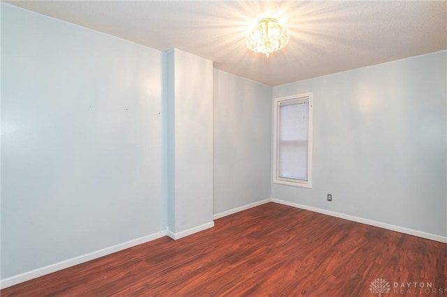 unfurnished room featuring dark wood-type flooring and an inviting chandelier