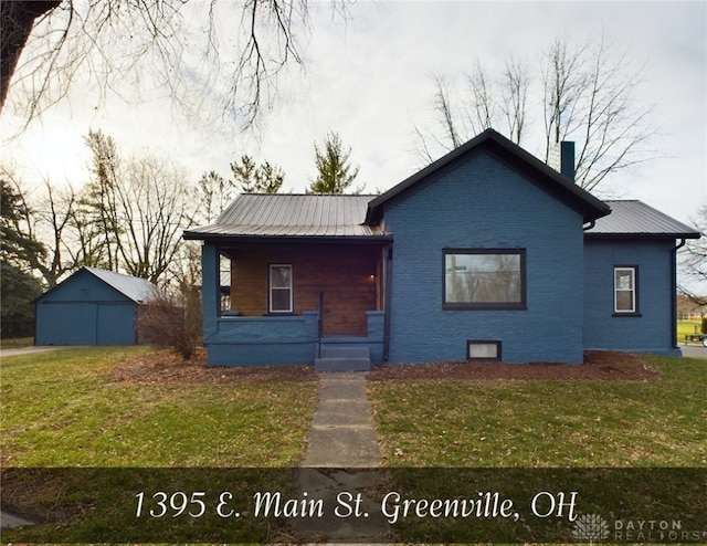 view of front of house with a front yard, a chimney, metal roof, and brick siding