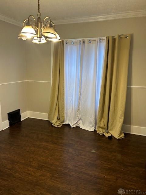 empty room featuring a chandelier, dark hardwood / wood-style floors, and crown molding