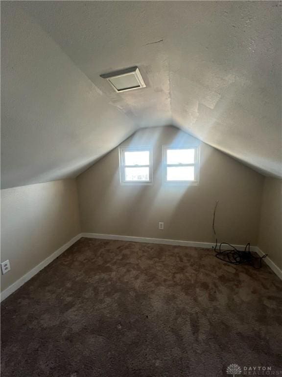 bonus room featuring lofted ceiling, dark carpet, and a textured ceiling