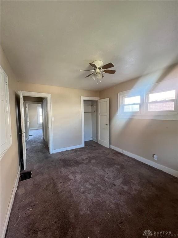 unfurnished bedroom featuring ceiling fan, dark carpet, and a closet