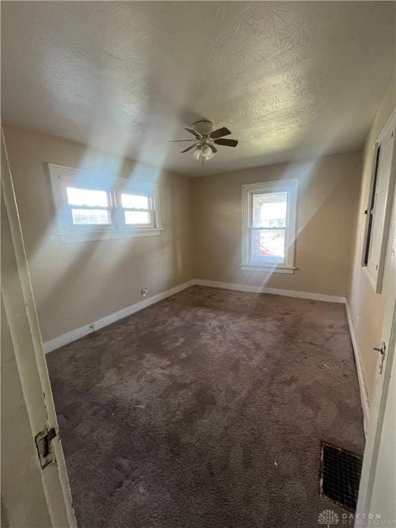 carpeted empty room with ceiling fan, plenty of natural light, and a textured ceiling