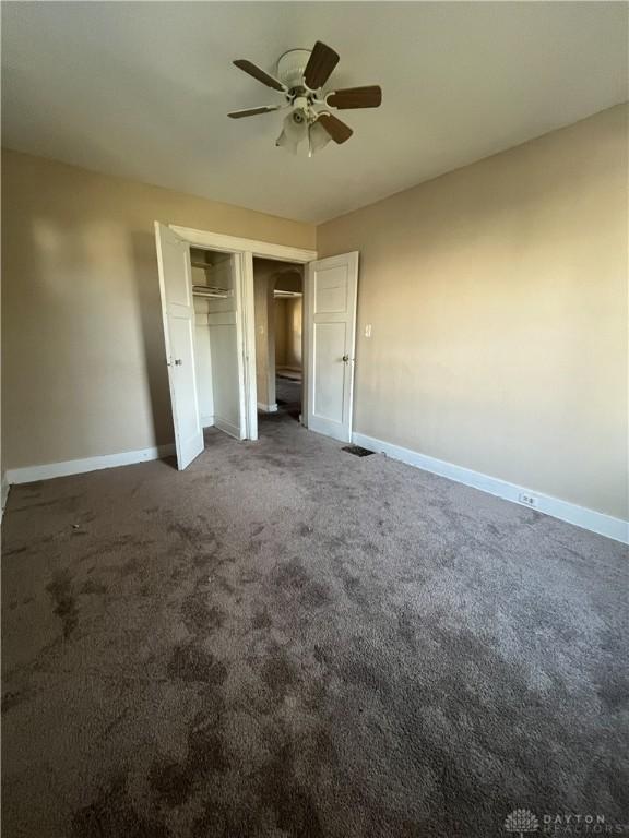 unfurnished bedroom with a closet, ceiling fan, and dark colored carpet