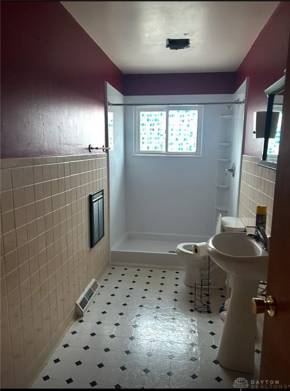 bathroom featuring toilet, a shower, and tile walls