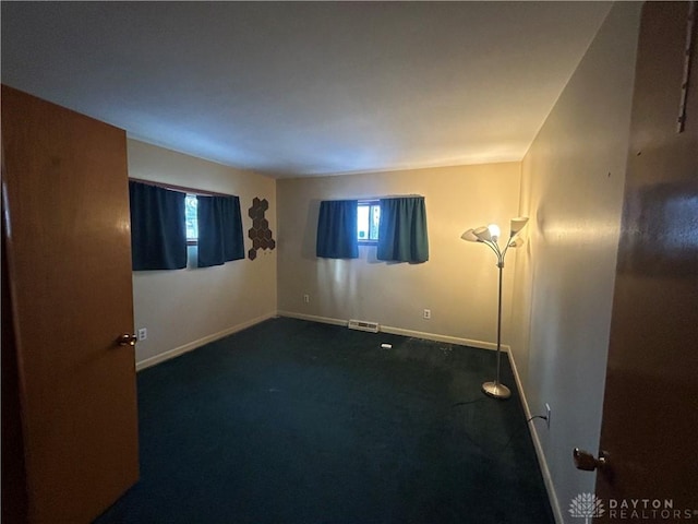 spare room featuring plenty of natural light and dark colored carpet