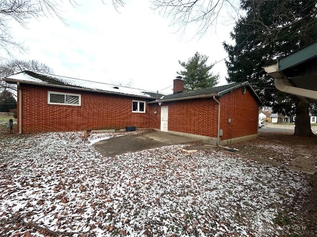 snow covered back of property with a patio area