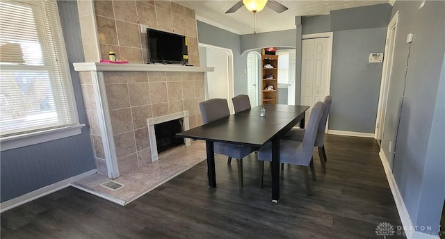 dining space featuring a tiled fireplace, ceiling fan, dark hardwood / wood-style flooring, and tile walls