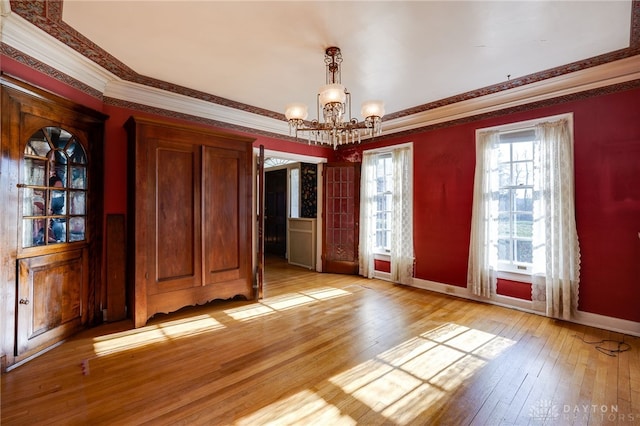 unfurnished dining area with a notable chandelier, light hardwood / wood-style floors, and ornamental molding