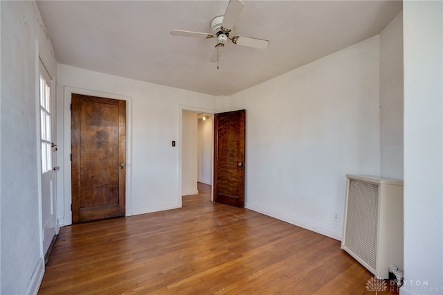 unfurnished bedroom featuring radiator, a closet, hardwood / wood-style flooring, and ceiling fan