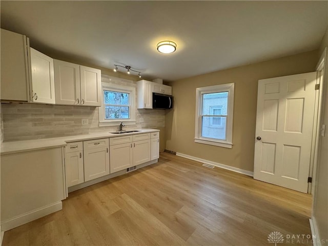 kitchen featuring white cabinets, rail lighting, sink, light hardwood / wood-style flooring, and decorative backsplash